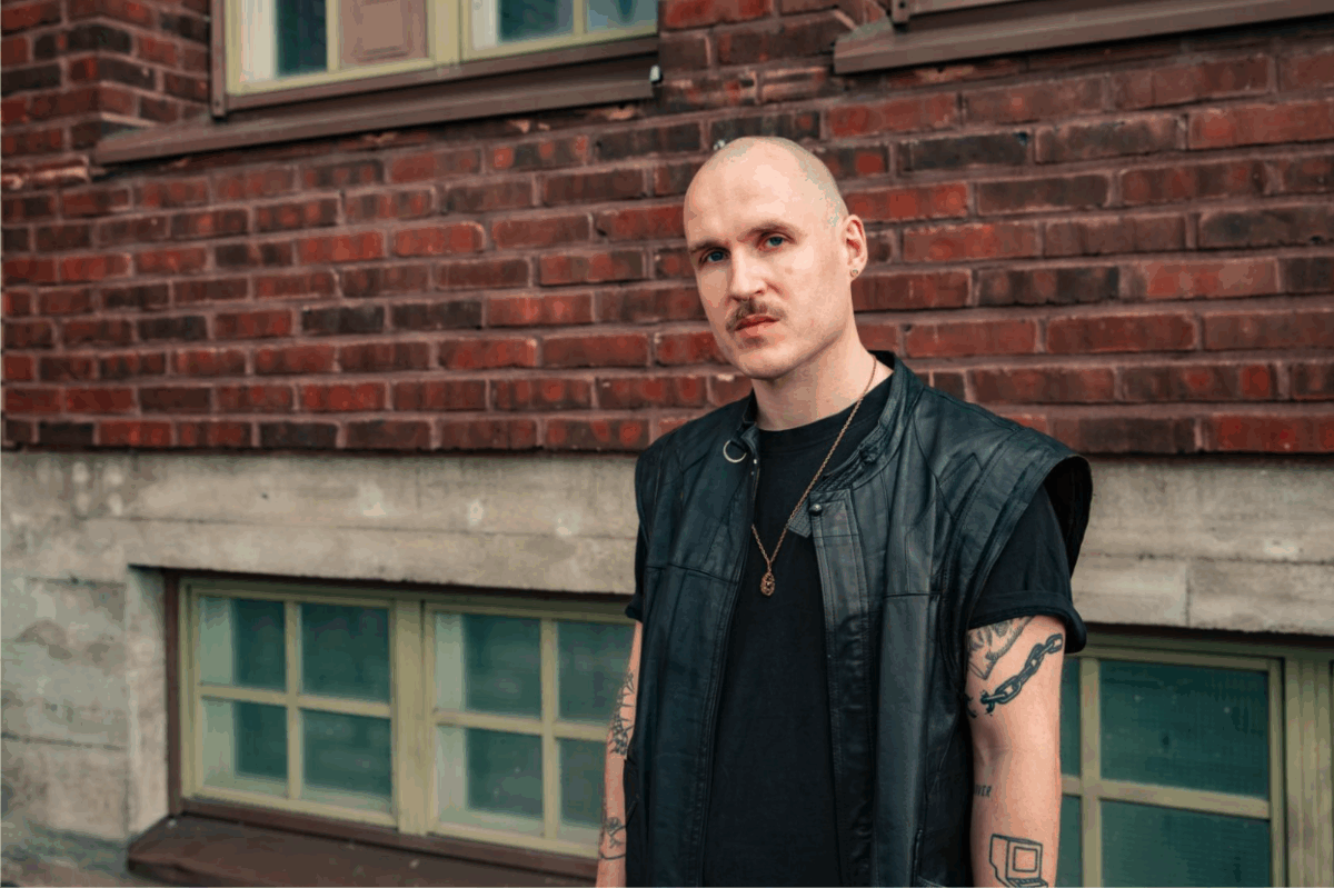 Ihminen mustassa nahkaliivissä tiiliseinän edessä.