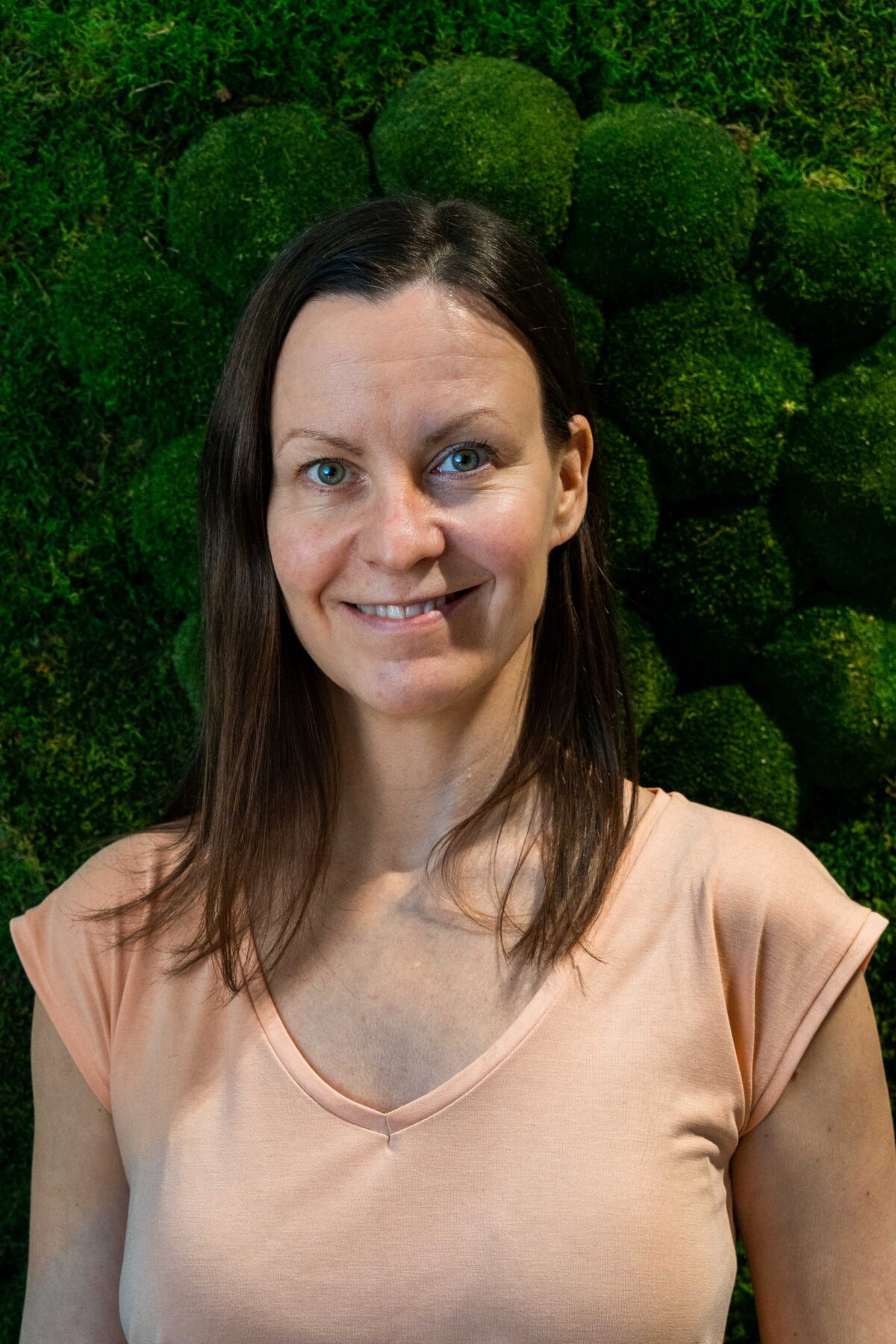 Hymyilevä nainen sammalseinän edessä.