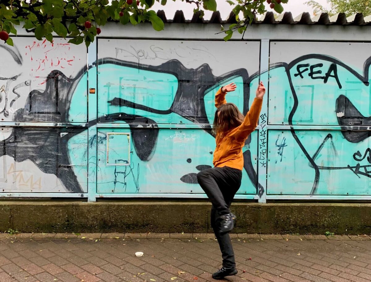 Nainen tanssii graffitiseinän edessä.